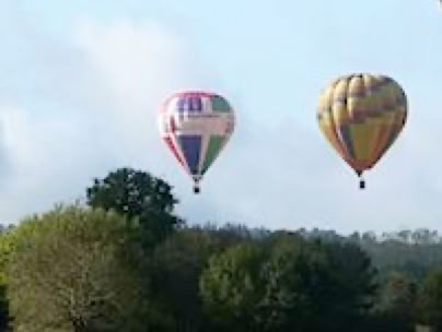 Deux mongolfières dans un ciel bleu et au dessus d'une forêt.